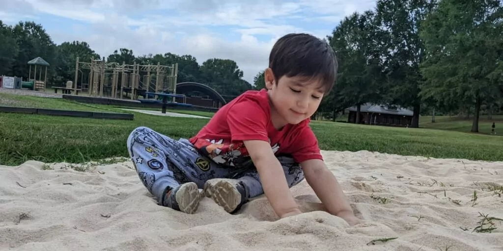 autistic child in a red shirt playing with sand